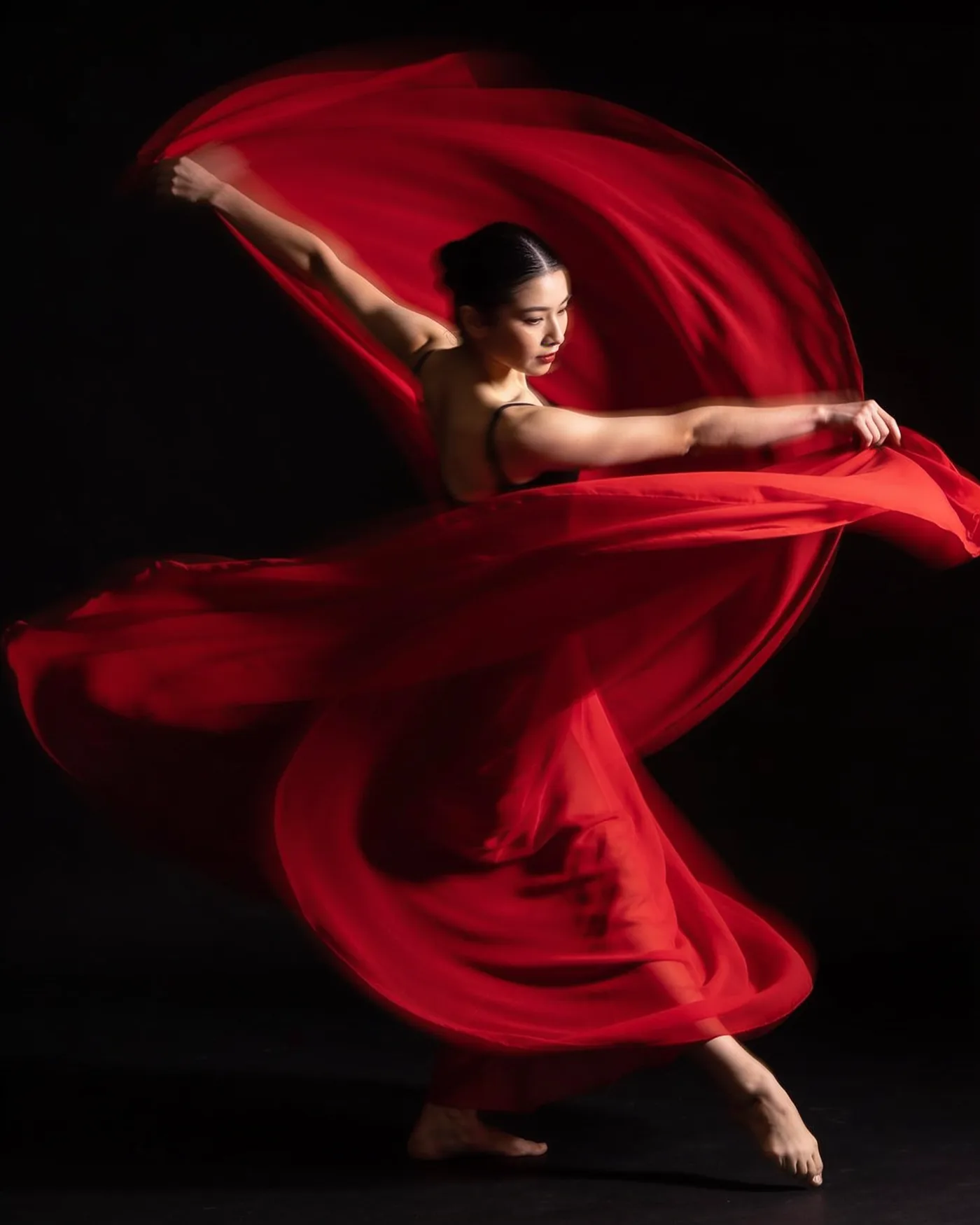 Image générée par Moqi à partir du texte : Portrait studio d'une danseuse en plein mouvement, un tissu rouge vole autour d'elle, fond noir, lumière dramatique.