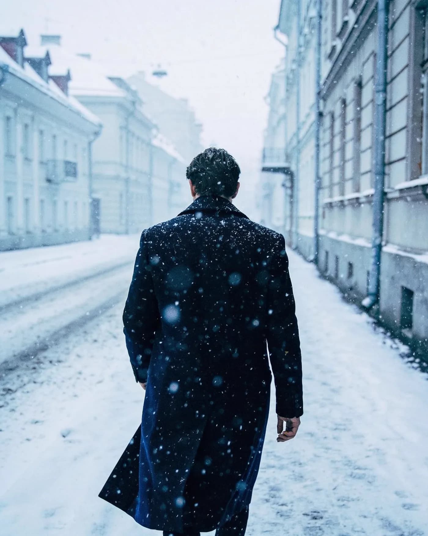 Image générée par Moqi à partir du texte : Photo de mode : un homme en long manteau marche dans une rue enneigée, tons froids, grain de pellicule.